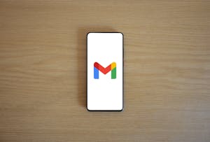 A smartphone displaying the Gmail app logo on a wooden surface, viewed from above.