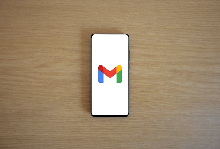 A smartphone displaying the Gmail app logo on a wooden surface, viewed from above.