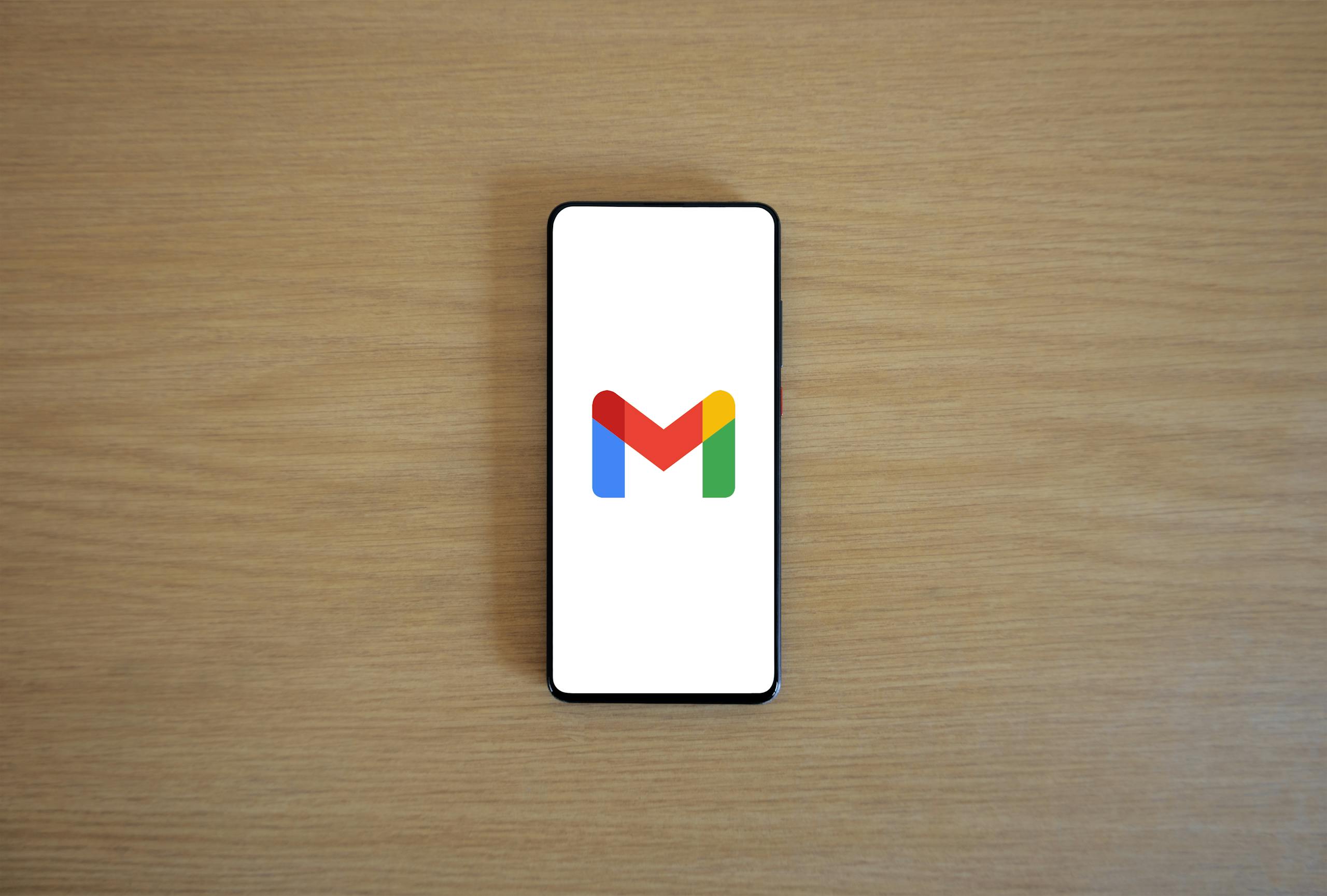 A smartphone displaying the Gmail app logo on a wooden surface, viewed from above.